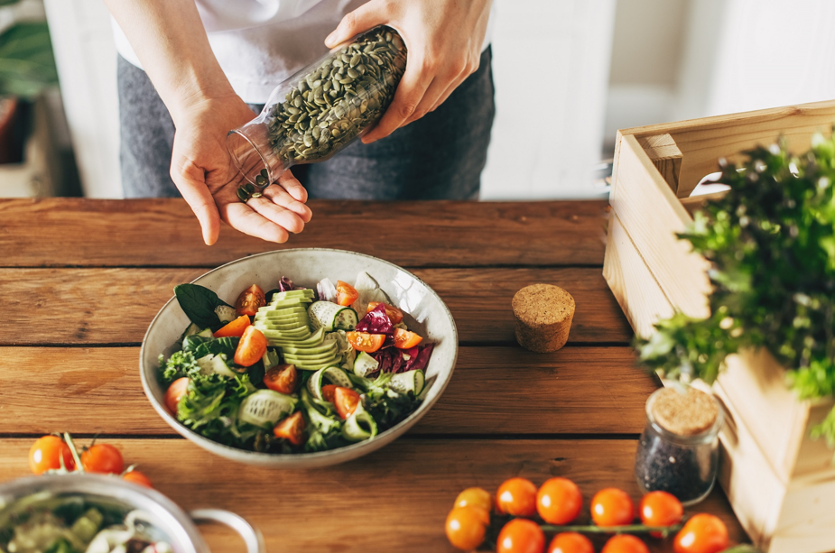 Une assiette de légumes garnie, avec une personne ajoutant des graines de courge par-dessus.