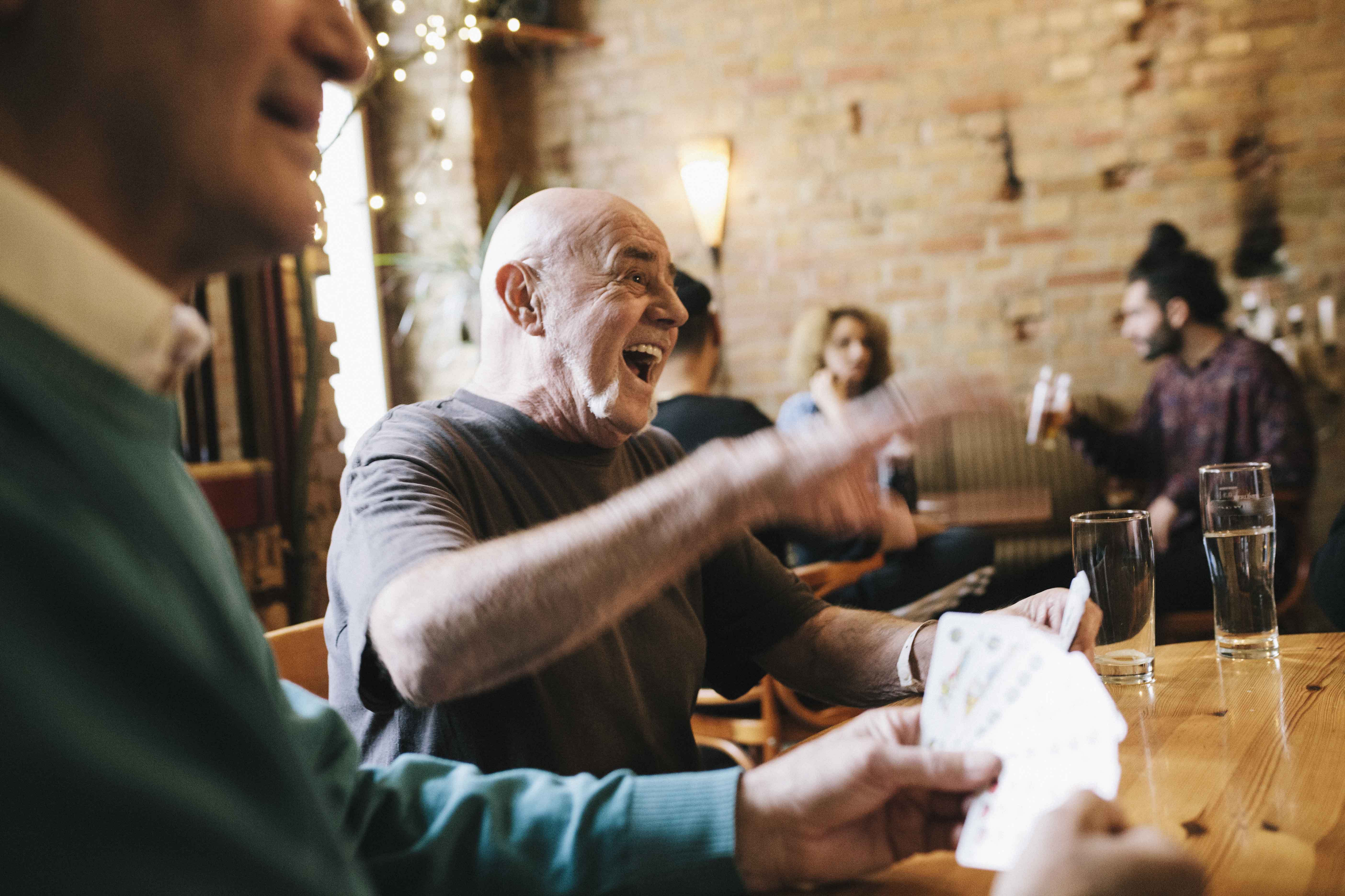 Un homme éclatant de rire, entouré d'autres personnes dans l'ambiance conviviale d'un café